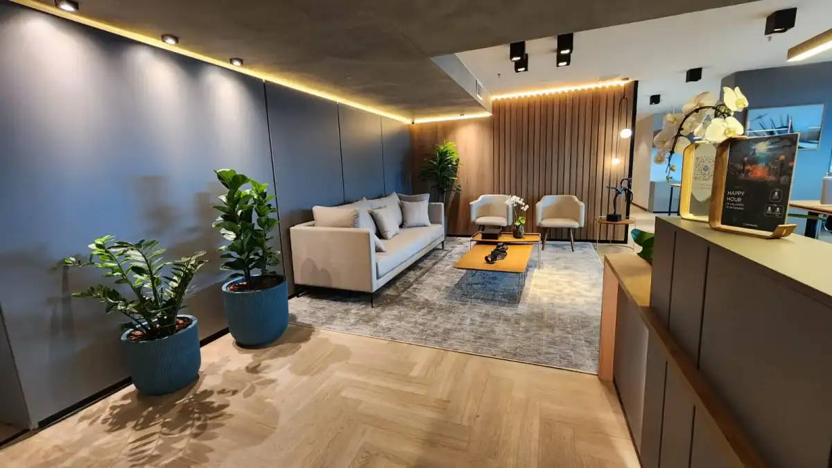 Recepção de um escritório personalizado com sofá, poltronas, painel ripado de madeira e iluminação indireta