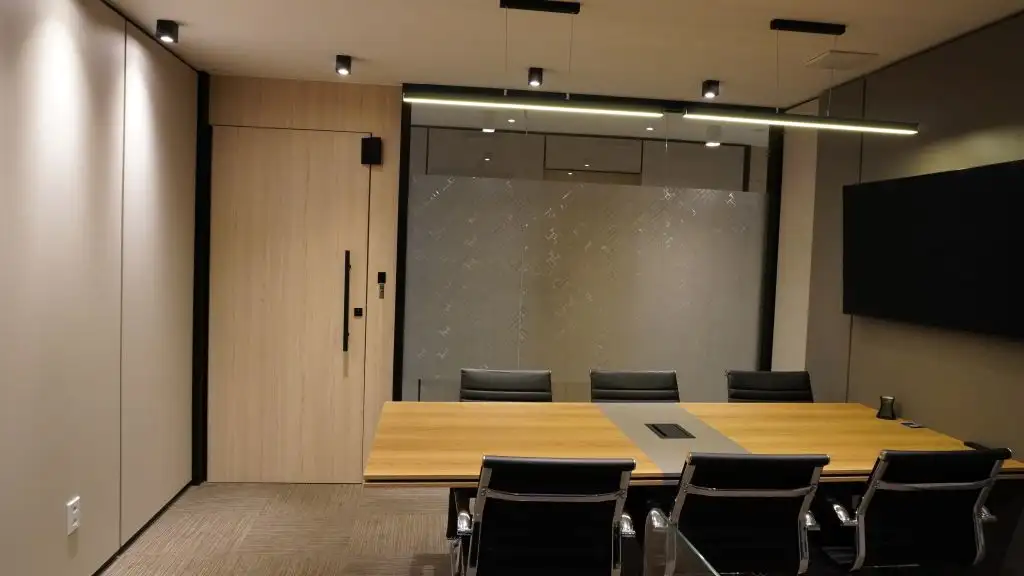 Sala de reunião com parede de vidro, painel de madeira, tela e cadeiras pretas