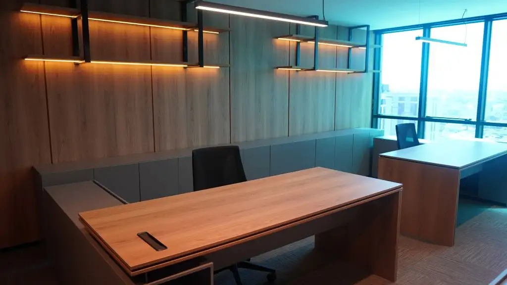 Sala de diretoria com mesa em madeira, estantes com luz embutida e janela para a cidade