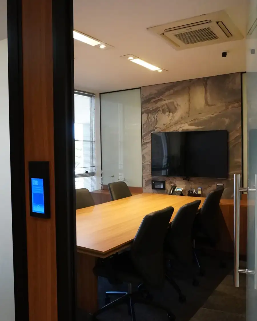 Sala de reunião da unidade Prime Business com mesa de madeira, painel de pedra e tela