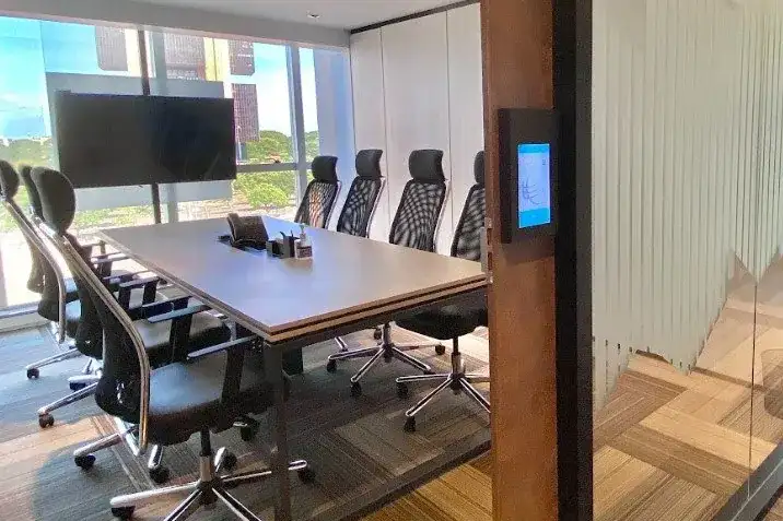 Sala de reunião da unidade Prime Business com divisórias de vidro, mesa branca e tela