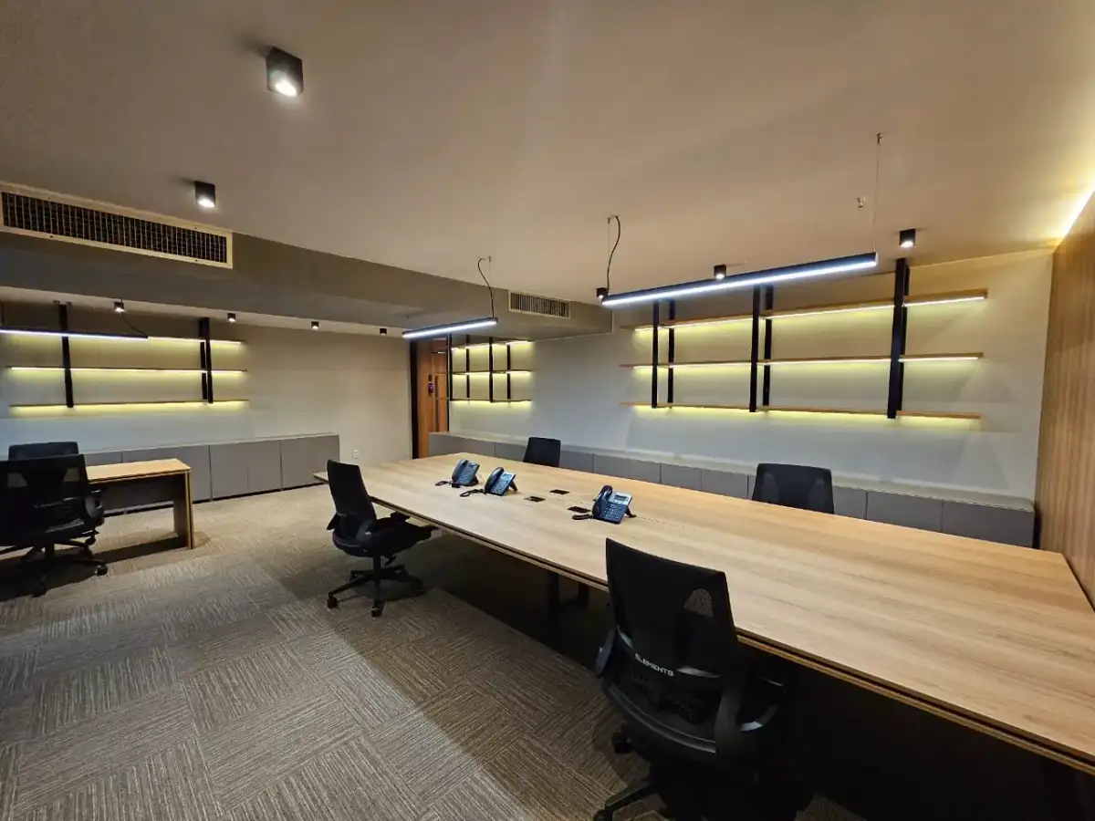 Sala de reunião de um escritório personalizado com mesa longa em madeira, estantes iluminadas e iluminação linear