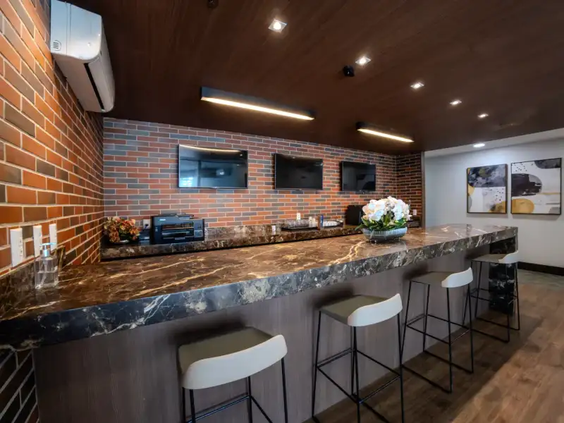 Café da unidade Nasa Business Style com bancada de mármore, banquetas, parede de tijolos e teto de madeira