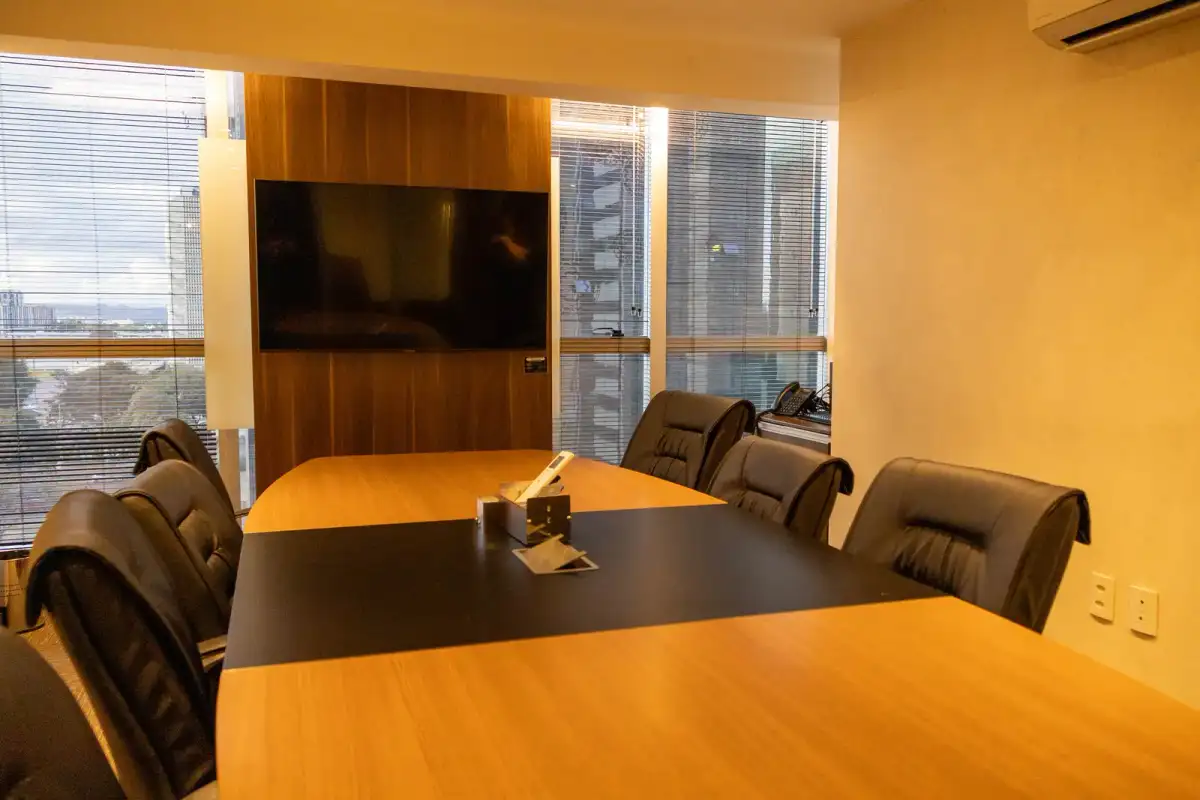 Sala de reunião da unidade Prime Business com mesa escura, cadeiras de couro, tela e janela para a cidade