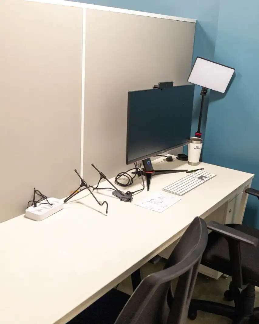 Interior de uma cabine fixa da unidade Prime Business, com mesa, monitor, iluminação para vídeo e duas cadeiras