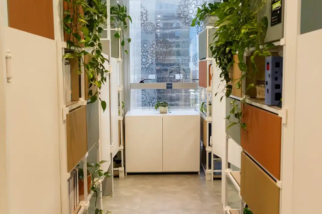 Corredor de cabines fixas da unidade Prime Business, com estantes de plantas e janela ao fundo