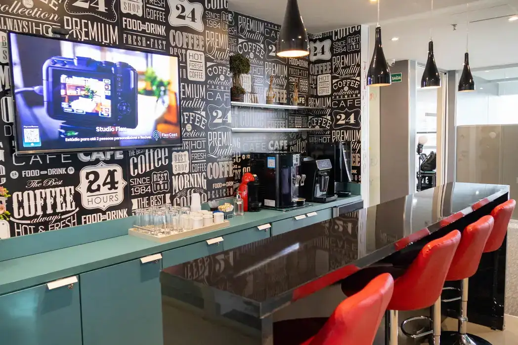 Café da unidade Prime Business com parede tipográfica, máquinas de café e banquetas vermelhas