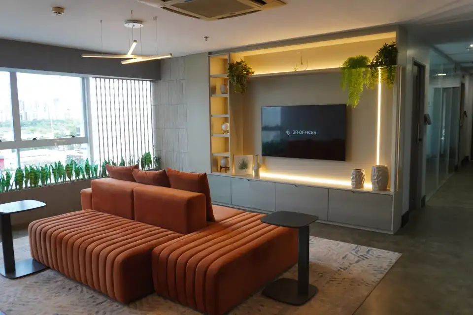Lounge da unidade Nasa Business Style em Goiânia com sofá laranja, painel de madeira iluminado e janelas para a cidade