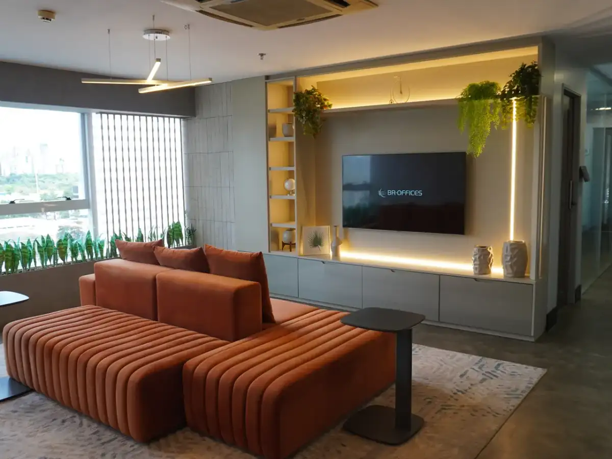 Lounge da unidade Nasa Business Style com sofá laranja, painel de madeira iluminado e janelas para a cidade