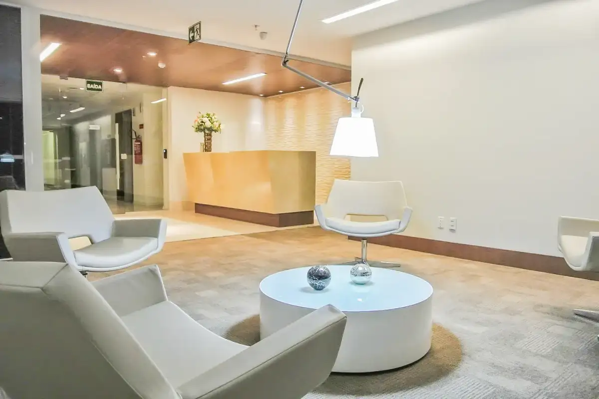Recepção da unidade Nasa Business Style com poltronas brancas, mesa de centro e balcão dourado ao fundo