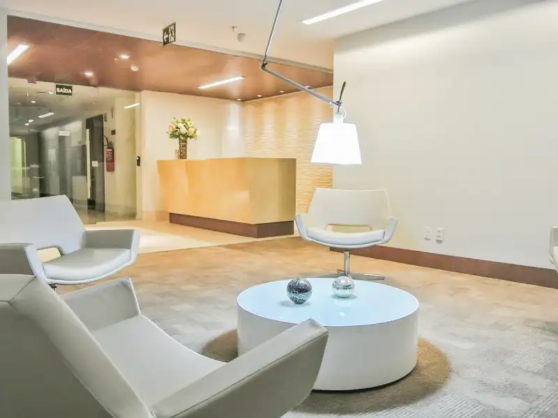 Recepção da unidade Nasa Business Style com poltronas brancas, mesa de centro e balcão dourado ao fundo