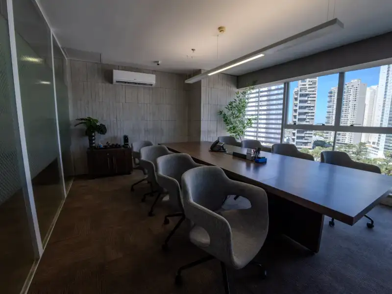 Sala de reunião da unidade Nasa Business Style com mesa longa de madeira e janelas para os prédios de Goiânia