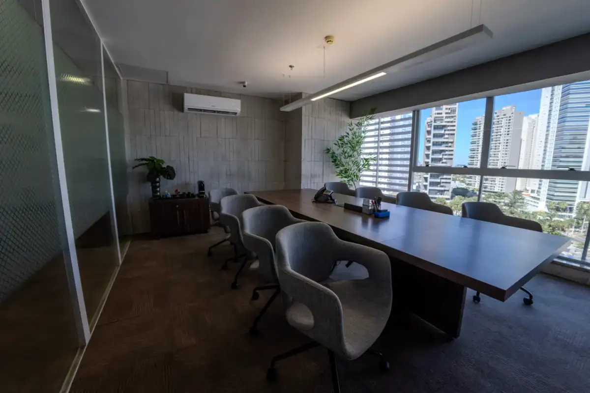 Sala de reunião da unidade Nasa Business Style com mesa longa de madeira, cadeiras cinza e janelas para os prédios de Goiânia