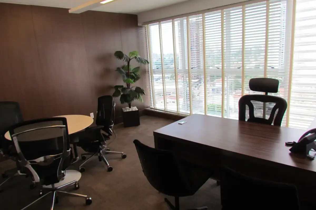 Escritório executivo da unidade Nasa Business Style com mesa de madeira, cadeiras de couro, mesa de reunião redonda e janelas para a cidade