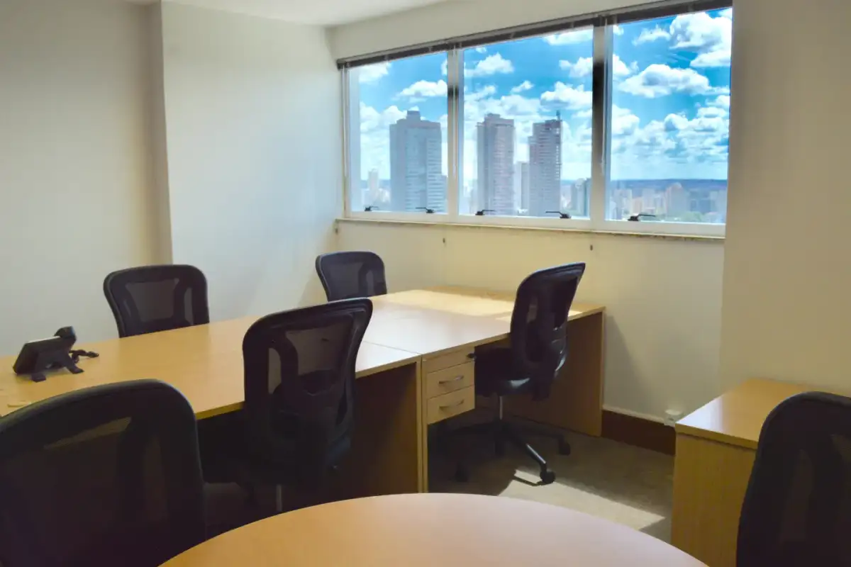 Escritório privativo da unidade Nasa Business Style com mesas, cadeiras pretas e janela com vista para os prédios de Goiânia