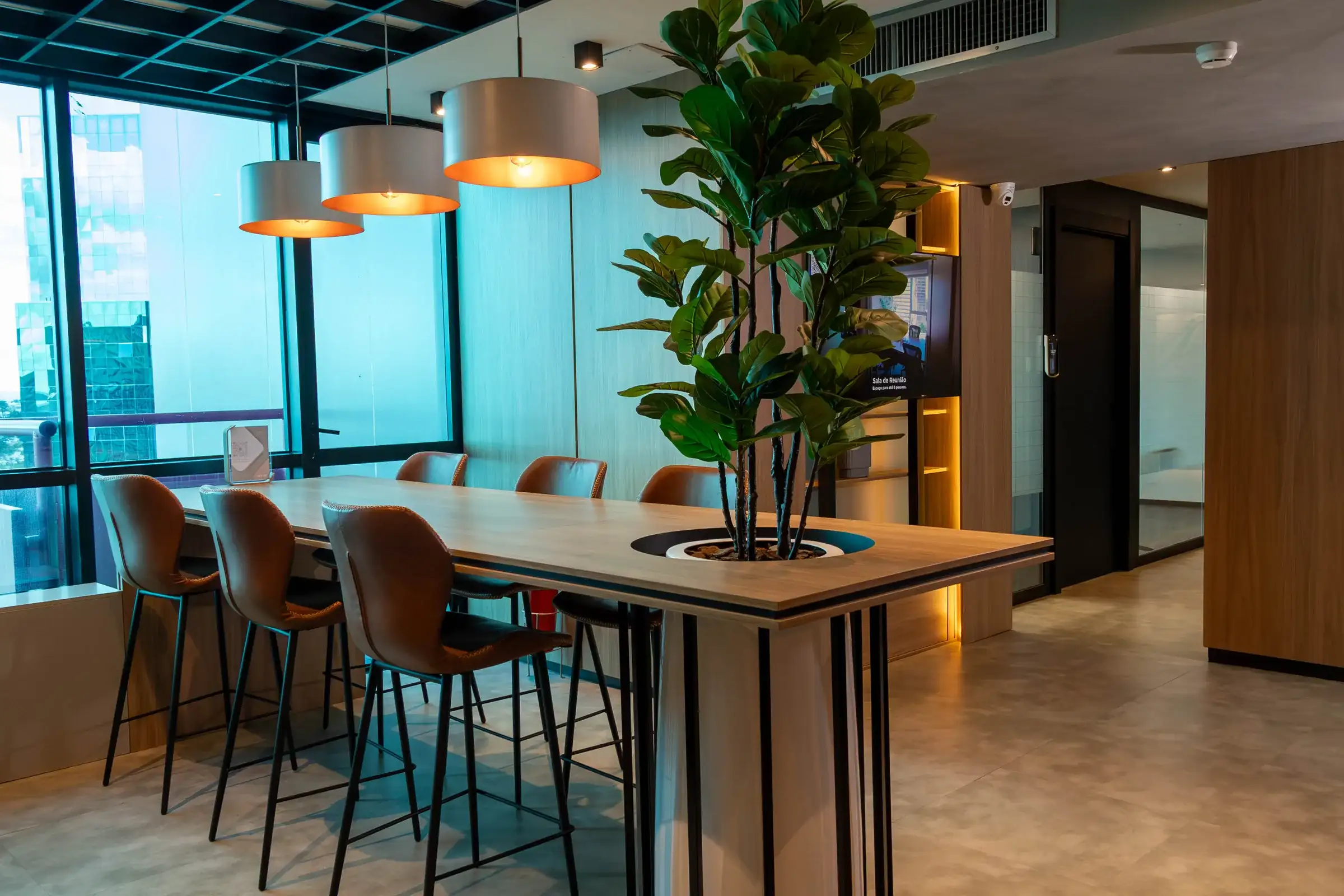 Espaço café da unidade Number One com mesa alta de madeira, banquetas de couro, luminárias pendentes e janelas para a cidade
