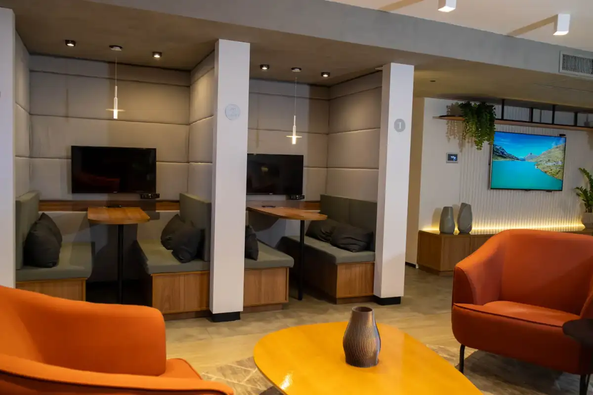 Lounge da unidade Number One com cabines estofadas, telas e poltronas laranja