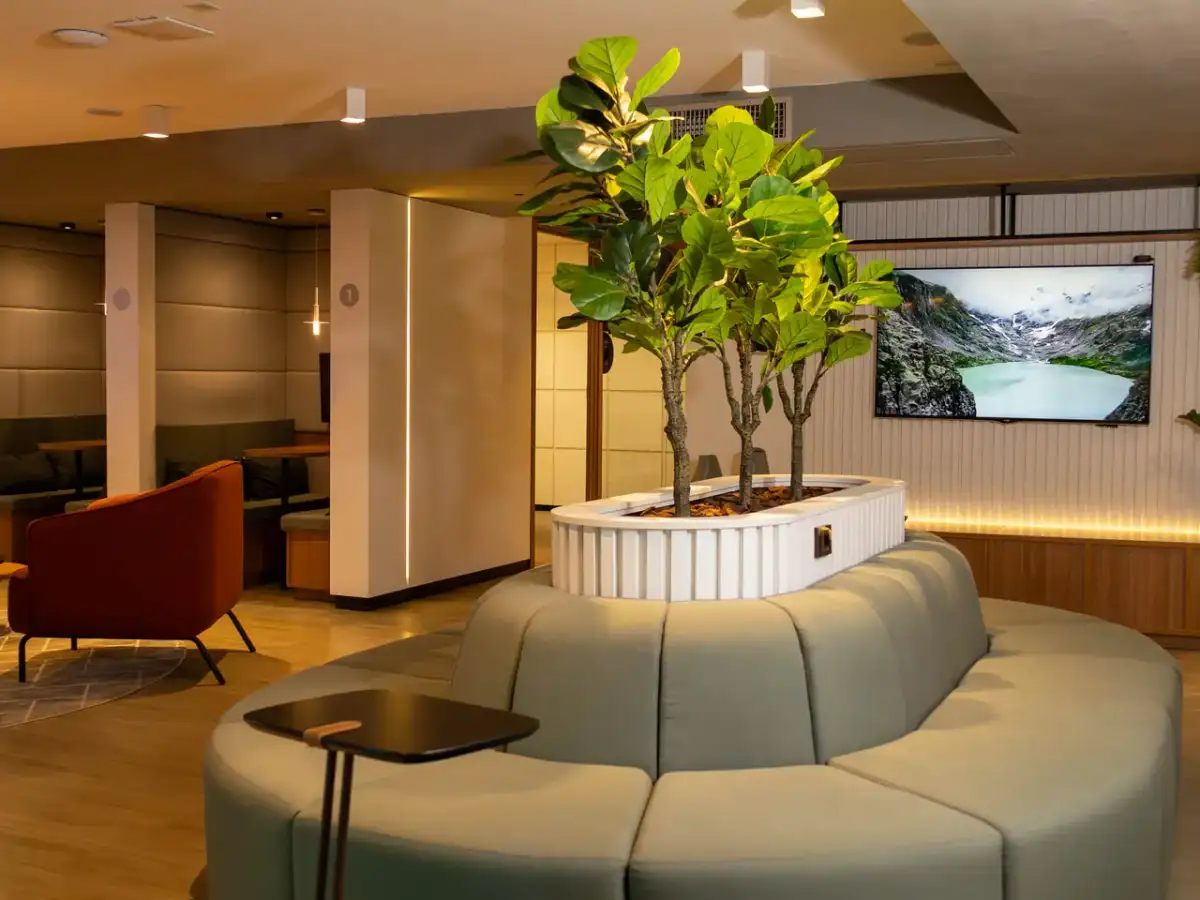 Lounge do 17º andar da unidade Number One com sofá circular, árvore ao centro e tela
