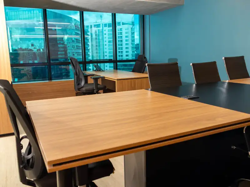 Escritório privativo da unidade Number One com mesas de madeira, parede azul e janelas para a cidade