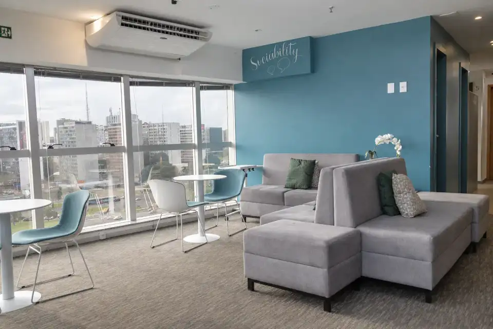 Lounge da unidade Prime Business com sofás claros, parede azul e janelas com vista para Brasília