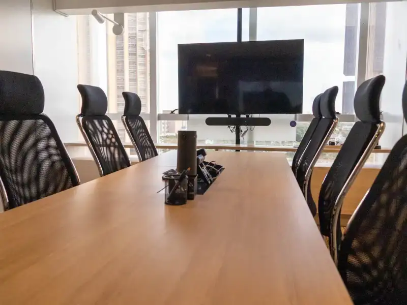 Sala de reunião da unidade Prime Business com mesa longa, cadeiras executivas e tela
