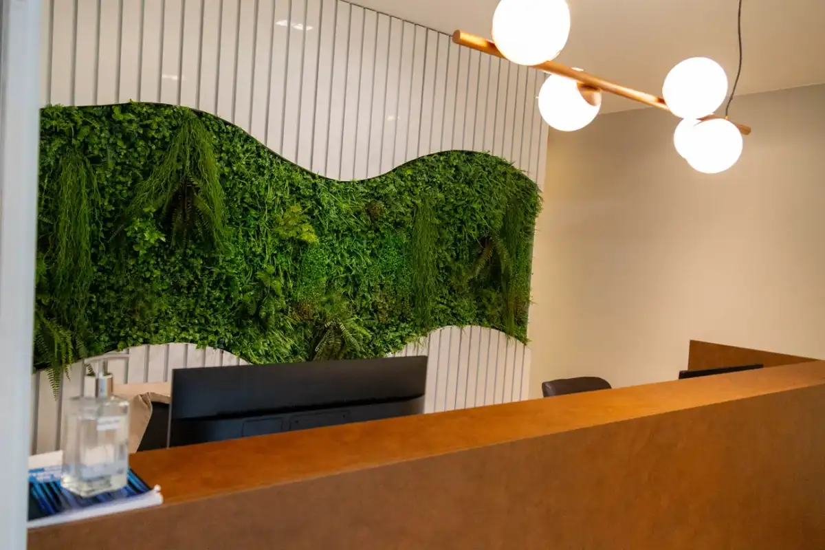 Recepção da unidade Prime Business com parede verde de plantas, balcão de madeira e luminárias redondas