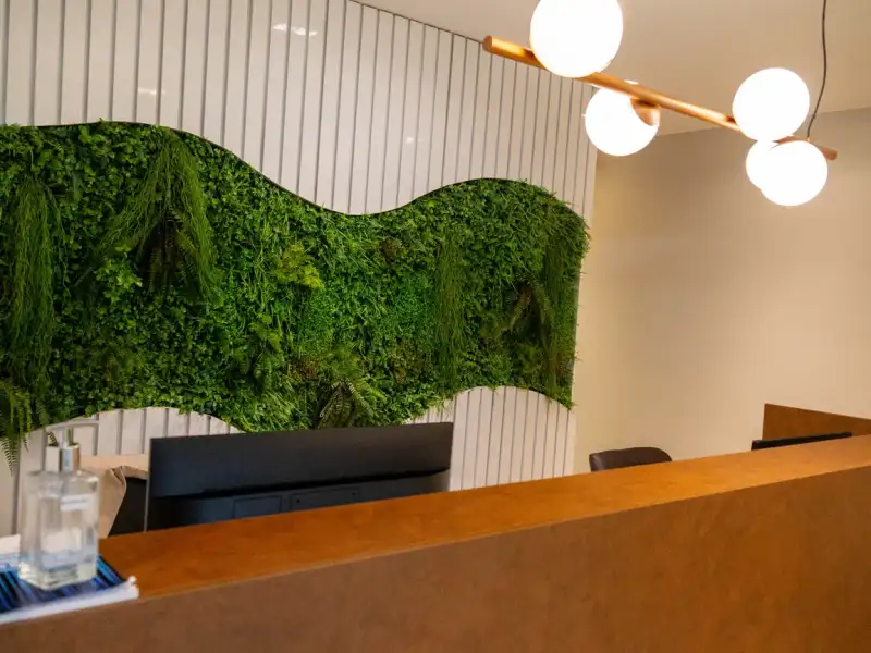 Recepção da unidade Prime Business com parede verde de plantas e balcão de madeira